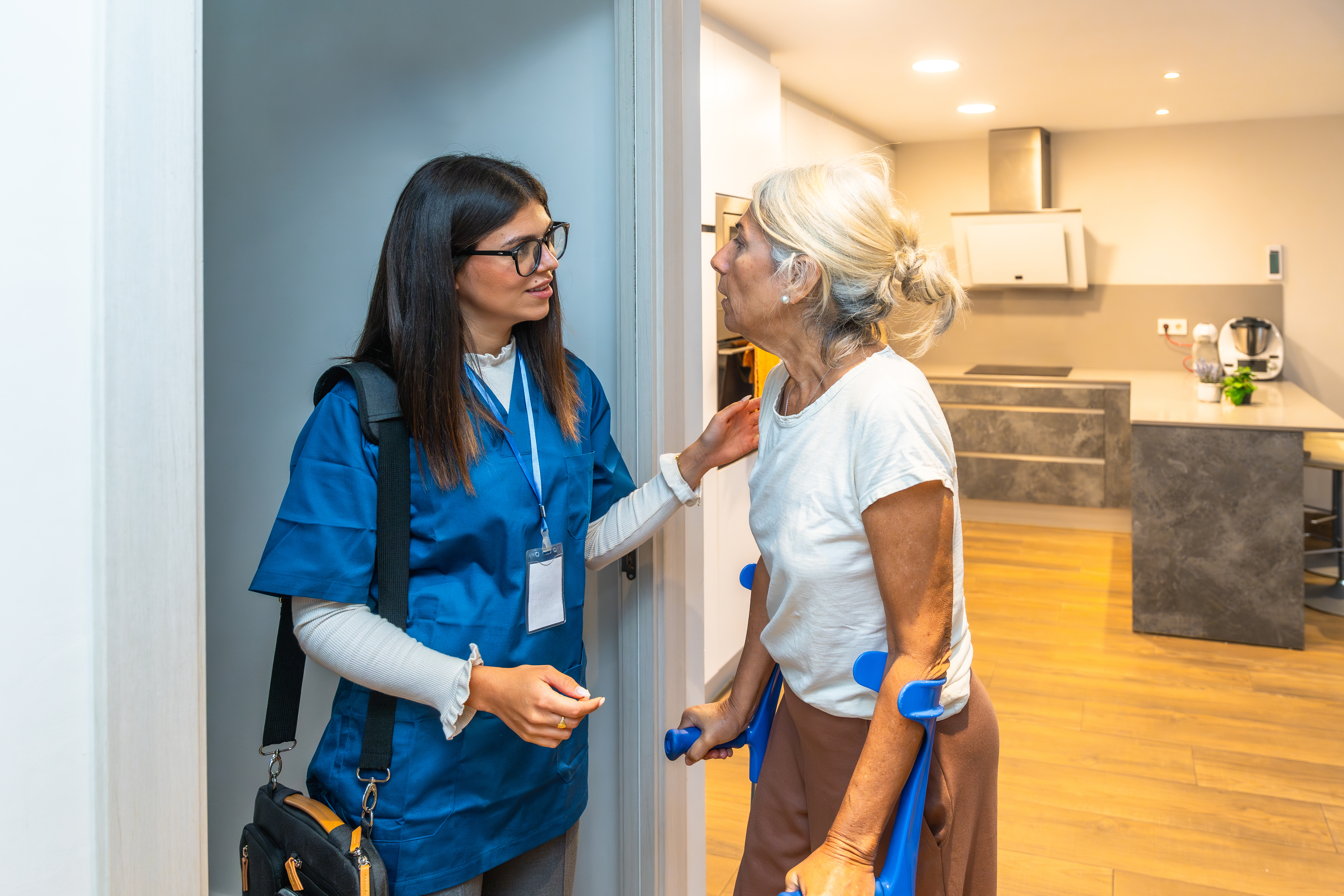 Healthcare worker visiting senior woman at home, offering support and guidance as she uses crutches during recovery, friendly conversation and practical home care assistance
